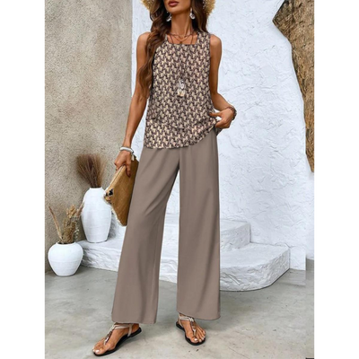 Femme en tenue estivale chic, portant un débardeur imprimé et un pantalon ample beige, accessoirisée d'un chapeau et d'un sac en paille.
