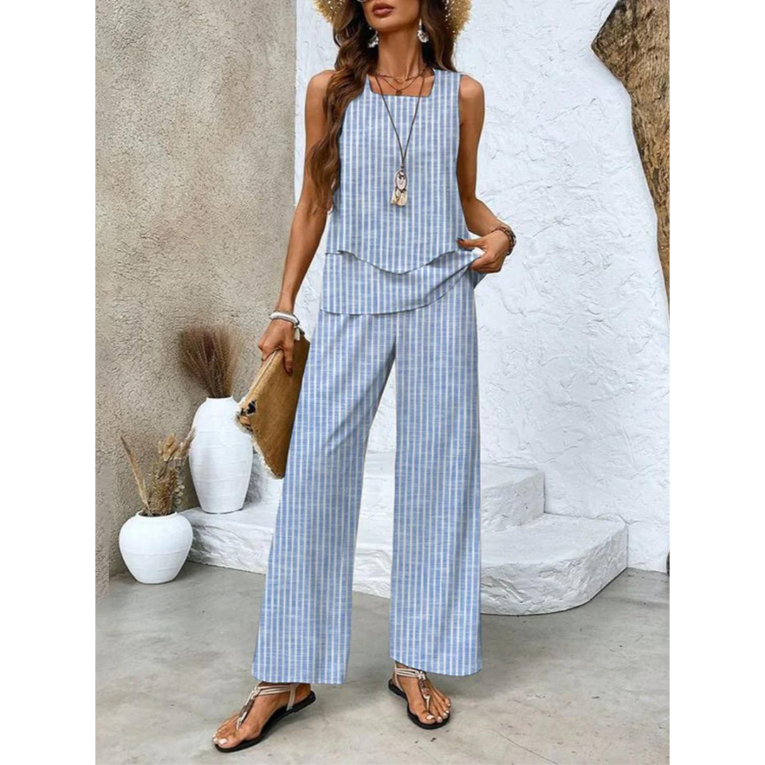 Femme en combinaison rayée bleue et blanche, chapeau de paille, sandales, tenant un sac en paille. Mode estivale chic, tendance décontractée.