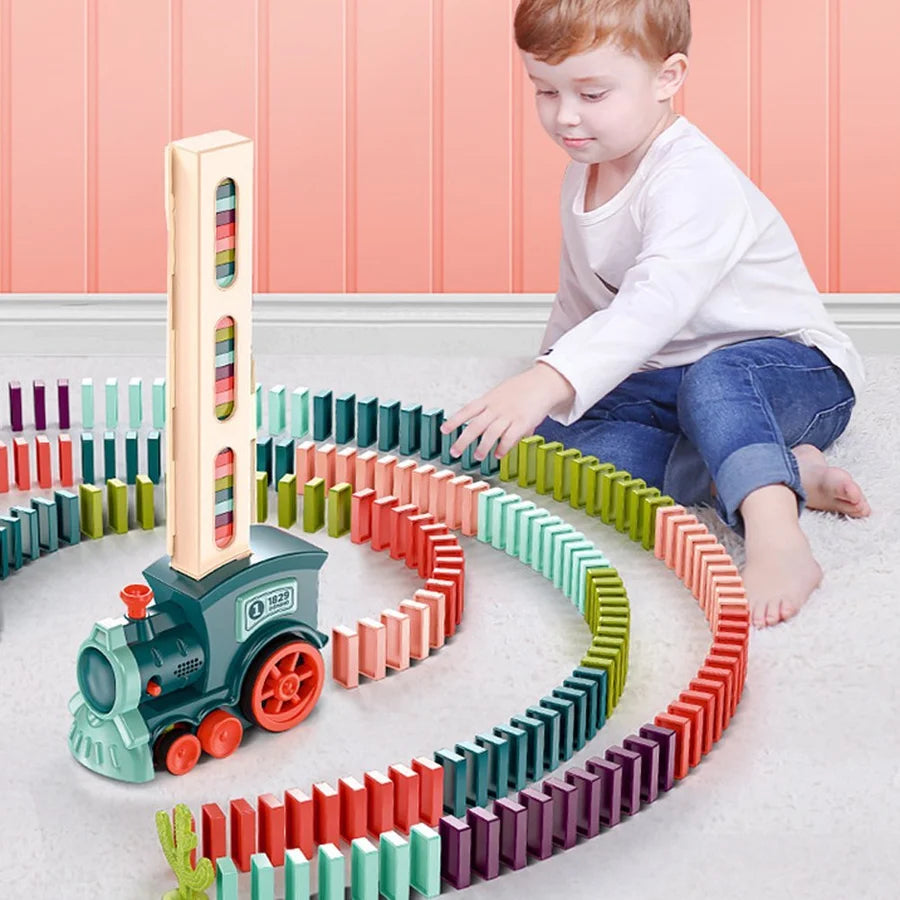 Enfant jouant avec un train domino coloré, empilant des dominos multicolores en cercle sur un tapis. Jouet éducatif pour développement créatif.