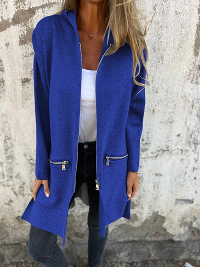 Femme portant un manteau bleu électrique avec fermetures éclair, sur fond de mur texturé. Mode automne, style décontracté, tendance urbaine.