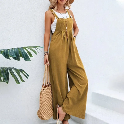 Femme en salopette jaune moutarde, chapeau de paille, sac en osier, posant près d'un mur blanc. Mode estivale décontractée, tendance et élégante.