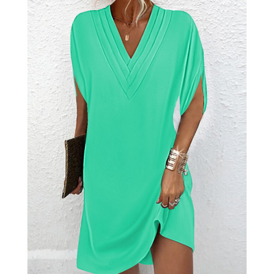 Robe verte élégante avec col en V, manches courtes, tenue d'été chic pour femme, accessoirisée d'un bracelet doré et d'une pochette marron.