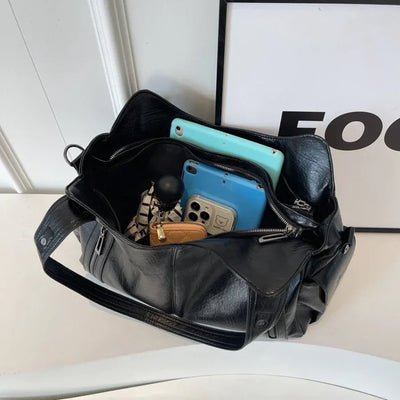 Sac à main noir en cuir ouvert, contenant un iPad, un iPhone, un portefeuille marron et des accessoires. Accessoires de mode, technologie, organisation.