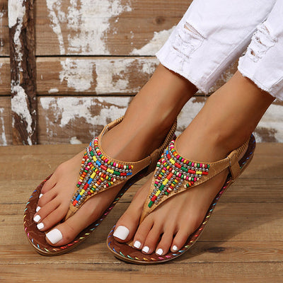 Sandales bohèmes à perles multicolores sur pieds féminins, posées sur un sol en bois. Mode estivale, chaussures tendance, style décontracté.
