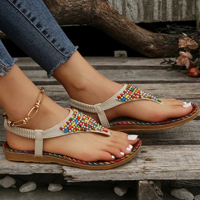 Sandales bohèmes à perles multicolores sur pieds féminins, posées sur un sol en bois. Chaussures d'été tendance, style décontracté et chic.