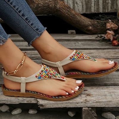 Sandales bohèmes à perles multicolores sur pieds féminins, posées sur un sol en bois. Chaussures d'été tendance, style décontracté et chic.