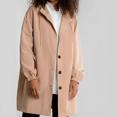 Personne portant un manteau beige à capuche, boutons noirs, sur une chemise blanche. Mode automne, style décontracté, vêtements tendance.