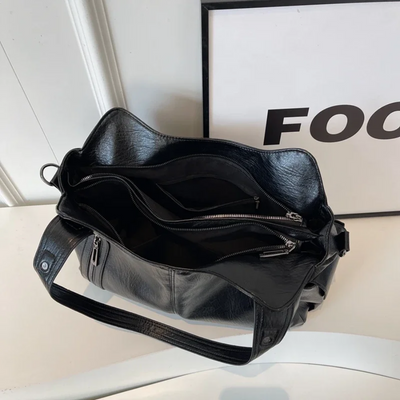 Sac à main en cuir noir ouvert avec fermetures éclair visibles, posé sur une surface blanche près d'un cadre. Accessoire de mode élégant et pratique.
