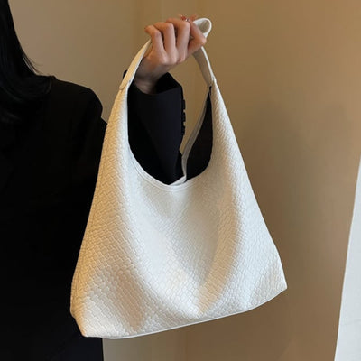 Sac à main blanc texturé, porté par une personne en veste noire. Design élégant et moderne, idéal pour la mode féminine et les accessoires tendance.