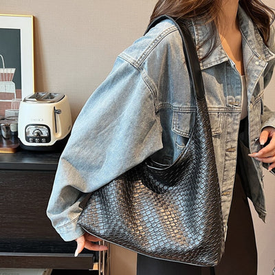 Femme portant un sac à main en cuir tressé noir, veste en jean, devant un grille-pain moderne. Mode tendance, accessoires élégants.