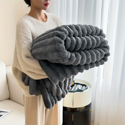 Femme tenant une couverture en fausse fourrure grise, douce et moelleuse, dans un salon moderne. Décoration intérieure cosy et élégante.
