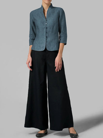 Femme portant une veste en lin bleu à manches trois-quarts et un pantalon large noir, posant sur fond gris. Mode élégante et minimaliste.