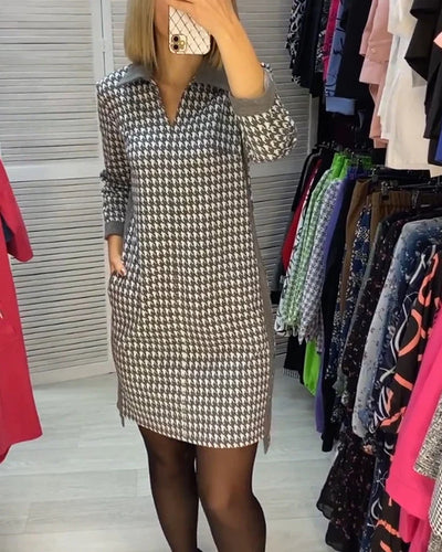 Robe à motif pied-de-poule noir et blanc, manches longues, portée par une femme dans une cabine d'essayage, entourée de vêtements colorés.