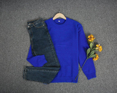Pull bleu vif sur cintre avec jean foncé, posé sur tapis gris, accompagné de fleurs jaunes. Mode automne, vêtements décontractés, style tendance.