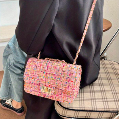 Sac à main en tweed multicolore avec chaîne dorée, porté par une personne en manteau noir. Accessoire mode élégant et tendance.