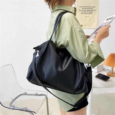Femme portant un grand sac à main noir en cuir, chemise verte, chaise transparente, lampe orange, lecture d'un magazine. Mode, accessoires, élégance.