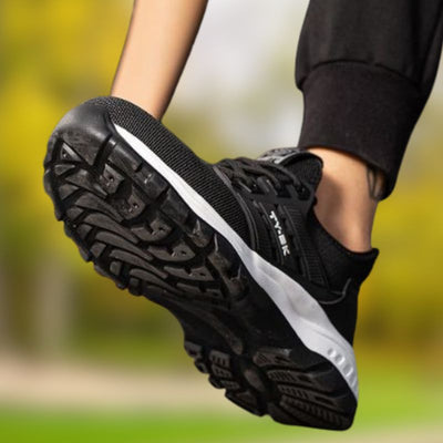 Chaussure de course noire avec semelle antidérapante, en mouvement sur fond flou de nature. Idéale pour sport et fitness en extérieur.