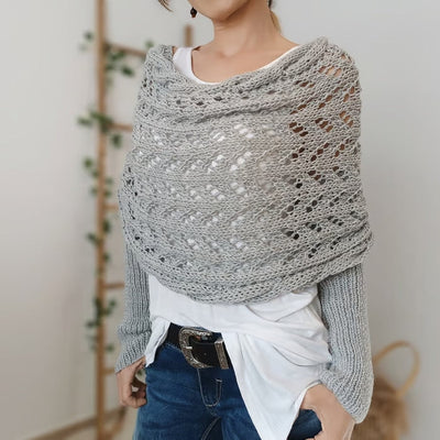 Femme portant un châle en tricot gris ajouré, style décontracté, sur un t-shirt blanc et un jean. Accessoire mode automne-hiver tendance.