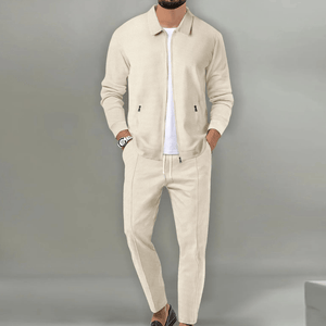 Homme portant un ensemble beige élégant, veste et pantalon assortis, style décontracté chic, montre au poignet, fond gris minimaliste.
