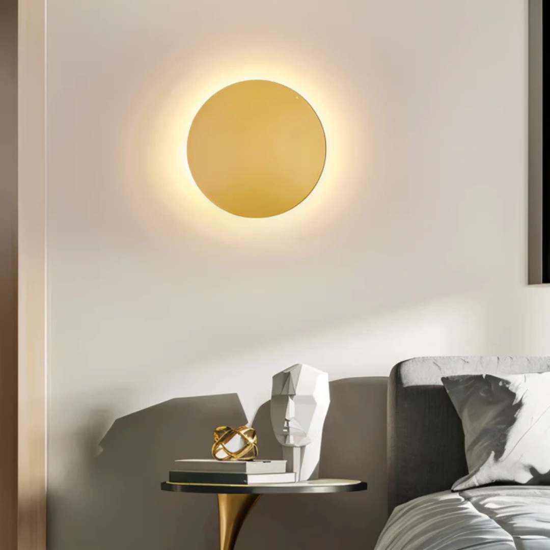 Miroir rond doré éclairé sur mur blanc, table d'appoint moderne avec sculpture géométrique et livres, chambre contemporaine élégante.