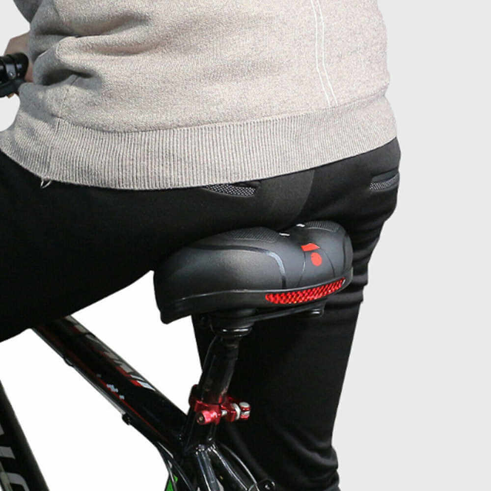 Homme en vélo avec selle ergonomique noire, coussin rembourré, lumière LED rouge. Confort cycliste, sécurité nocturne, équipement vélo moderne.
