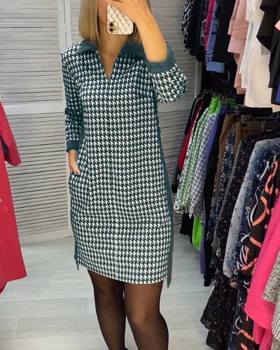 Femme portant une robe à motif pied-de-poule dans une cabine d'essayage, entourée de vêtements colorés. Mode, shopping, tendance.