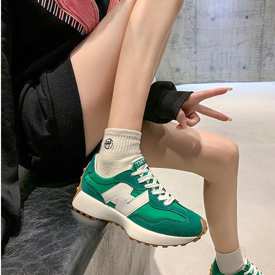 Chaussures de sport vertes et blanches sur fond urbain, portées avec des chaussettes blanches. Style moderne et tendance pour la mode urbaine.