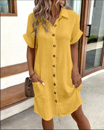 Robe chemise jaune à boutons en lin, manches courtes, portée par une femme avec sac en osier. Mode estivale décontractée, tendance et élégante.