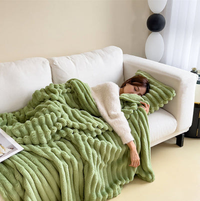 Femme endormie sur canapé blanc avec couverture en fausse fourrure verte, coussin assorti, intérieur moderne, détente, confort, salon élégant.