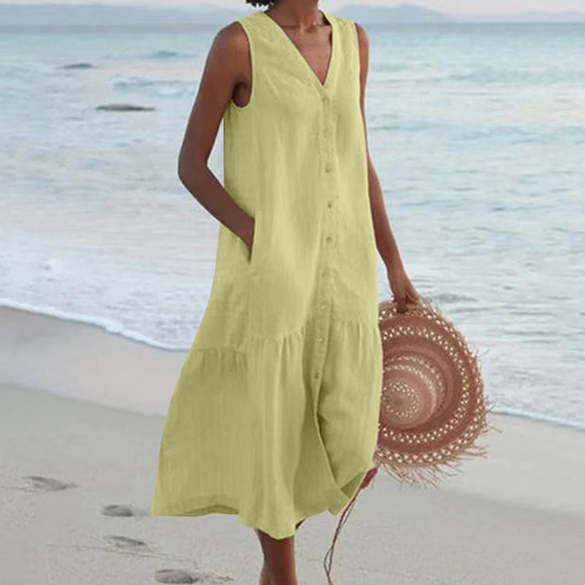 Robe d'été longue jaune sans manches, femme tenant un chapeau de paille, marchant sur une plage au bord de la mer. Mode plage élégante.