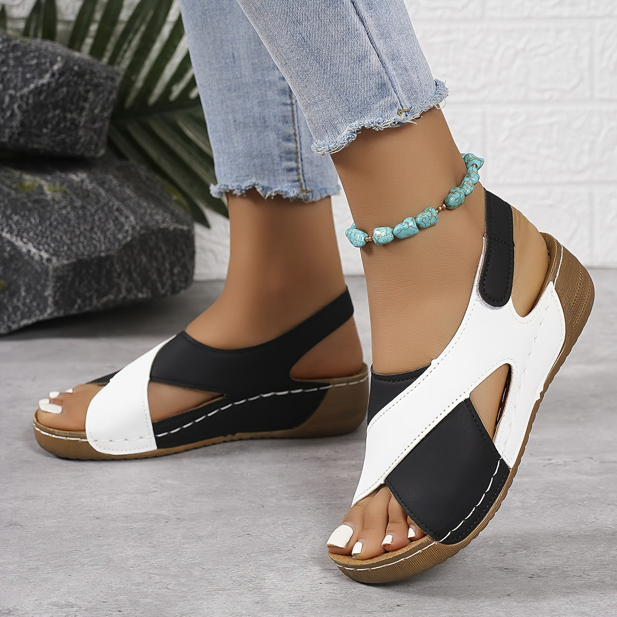 Sandales compensées noires et blanches pour femme, portées avec un jean clair. Accessoire: bracelet de cheville turquoise. Mode estivale décontractée.