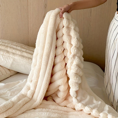 Couverture en fausse fourrure beige, douce et moelleuse, tenue par une main sur un lit. Décoration intérieure, confort, literie élégante.