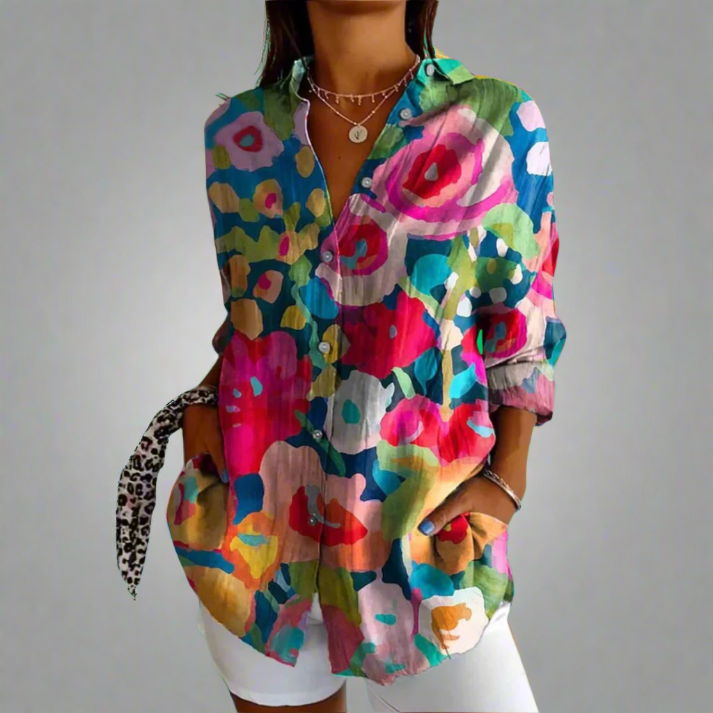 Chemise femme colorée à motifs floraux abstraits, manches longues, col ouvert, portée avec un pantalon blanc. Mode tendance, style décontracté.