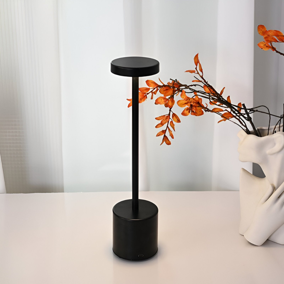 Lampe de table noire moderne sur bureau blanc, décorée de branches d'automne orange. Design minimaliste, éclairage intérieur élégant.