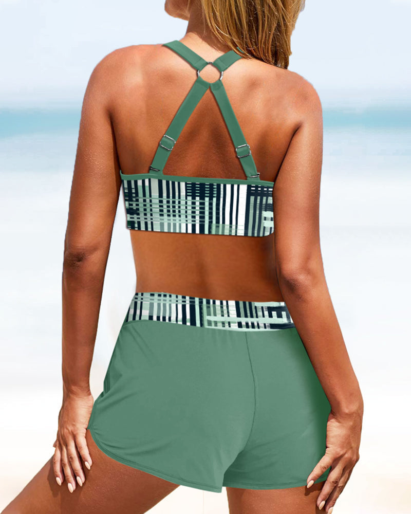 Femme en maillot de bain vert à motifs géométriques, dos à la caméra, sur une plage ensoleillée. Mode plage, tenue d'été, vacances mer.