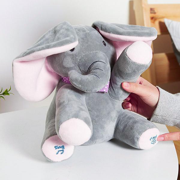 Peluche éléphant gris avec oreilles roses, tenue par une main. Jouet doux pour enfants, idéal pour câlins et décoration de chambre.