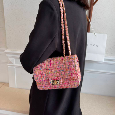 Sac à main en tweed multicolore porté par une femme en manteau noir, avec chaîne dorée, devant un mur blanc. Accessoire mode élégant et tendance.