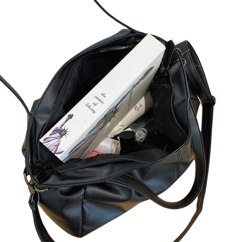 Sac à main noir en cuir ouvert contenant un livre, une montre, et des produits de beauté. Accessoire mode femme, élégant et pratique.