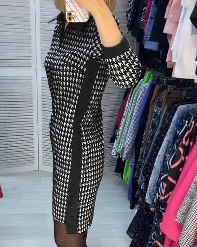 Robe à motif pied-de-poule noir et blanc, manches longues, portée par une femme dans une boutique de vêtements, entourée de divers vêtements colorés.