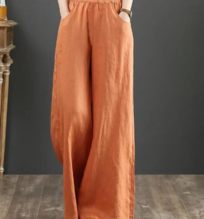 Pantalon large en lin orange pour femme, taille élastique, style décontracté, mode automne, sur fond gris et sol en bois.