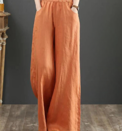 Pantalon large en lin orange pour femme, taille élastique, style décontracté, mode automne, sur fond gris et sol en bois.