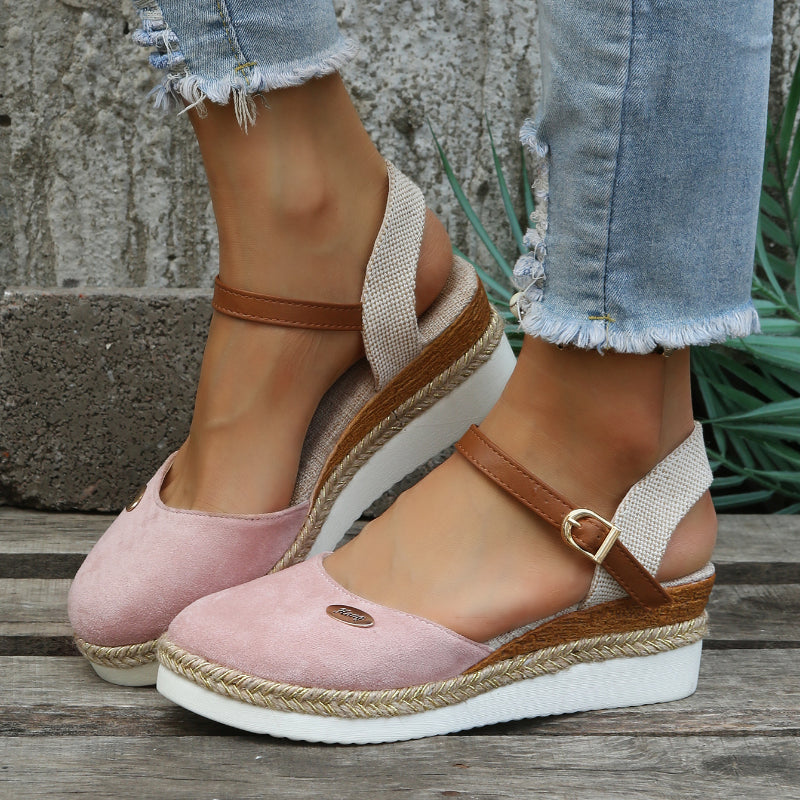 Sandales compensées roses pour femme avec bride marron, semelle en corde tressée, portées avec un jean déchiré. Mode estivale tendance.