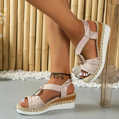 Sandales compensées rose doré pour femme, avec semelle en corde tressée et talon blanc, portées avec un bracelet de cheville, sur fond de bambou.