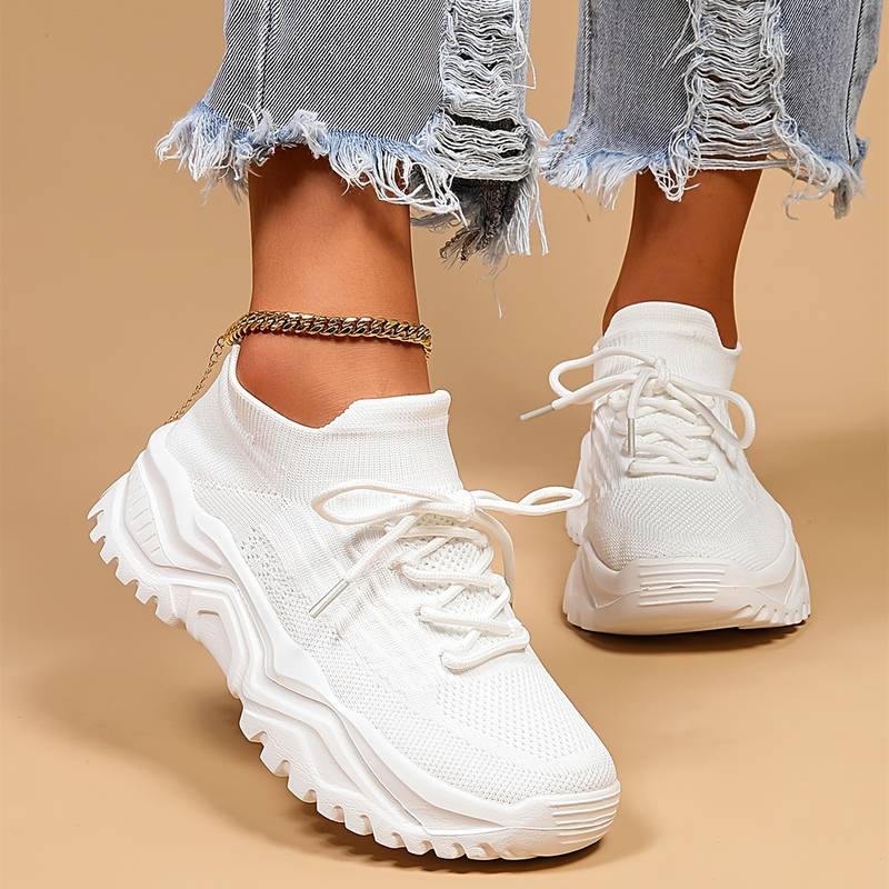 Baskets blanches tendance avec semelle épaisse, portées avec un jean déchiré. Chaussures de sport modernes pour femme, style décontracté.