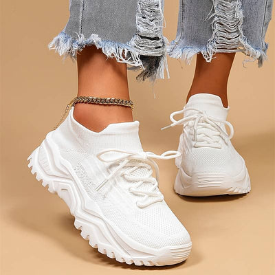 Baskets blanches tendance avec semelle épaisse, portées avec un jean déchiré. Chaussures de sport modernes pour femme, style décontracté.