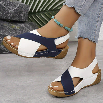 Sandales compensées bicolores bleu et blanc pour femme, avec semelle en bois, portées avec un jean déchiré et un bracelet turquoise.