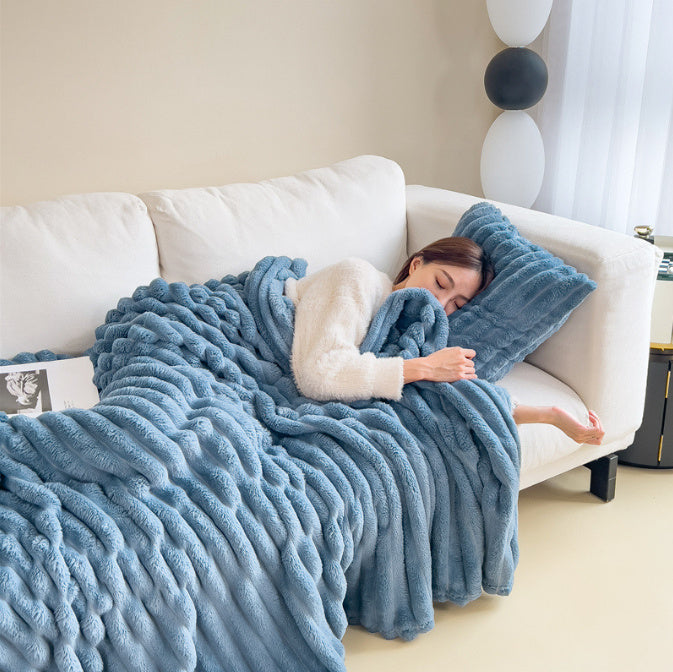Femme endormie sur un canapé blanc, enveloppée dans une couverture en fausse fourrure bleue. Décor moderne, ambiance cosy et relaxante.