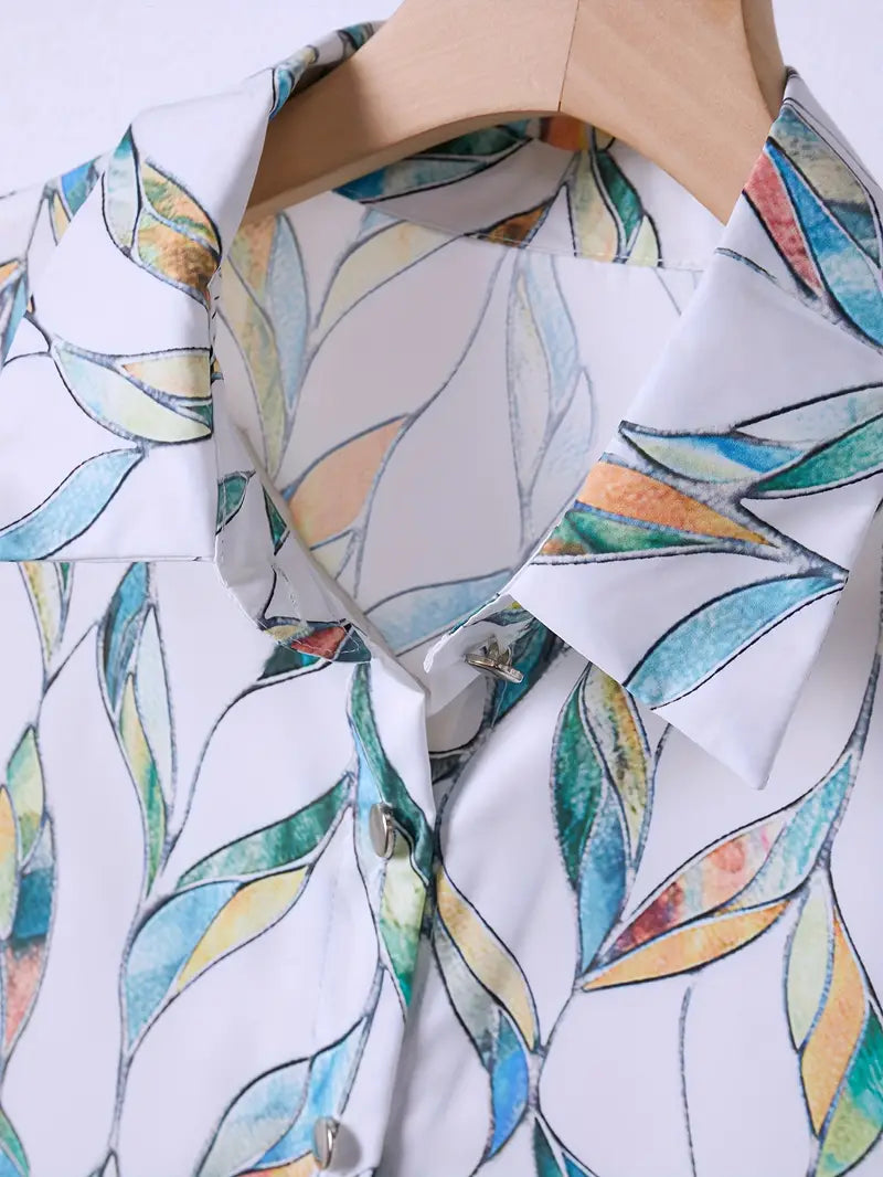 Chemisier en soie imprimé feuilles colorées, col classique, boutons nacrés, suspendu sur cintre en bois. Mode élégante et tendance.