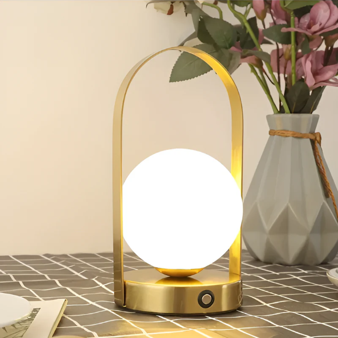 Lampe de table LED dorée moderne sur une nappe à carreaux, avec vase de fleurs en arrière-plan. Éclairage décoratif intérieur élégant et design.