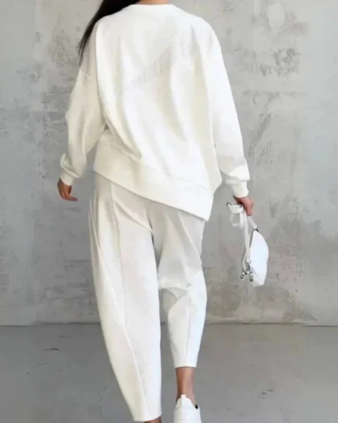 Femme en tenue décontractée blanche, portant un sweat et un pantalon ample, tenant un petit sac blanc. Style minimaliste et moderne.